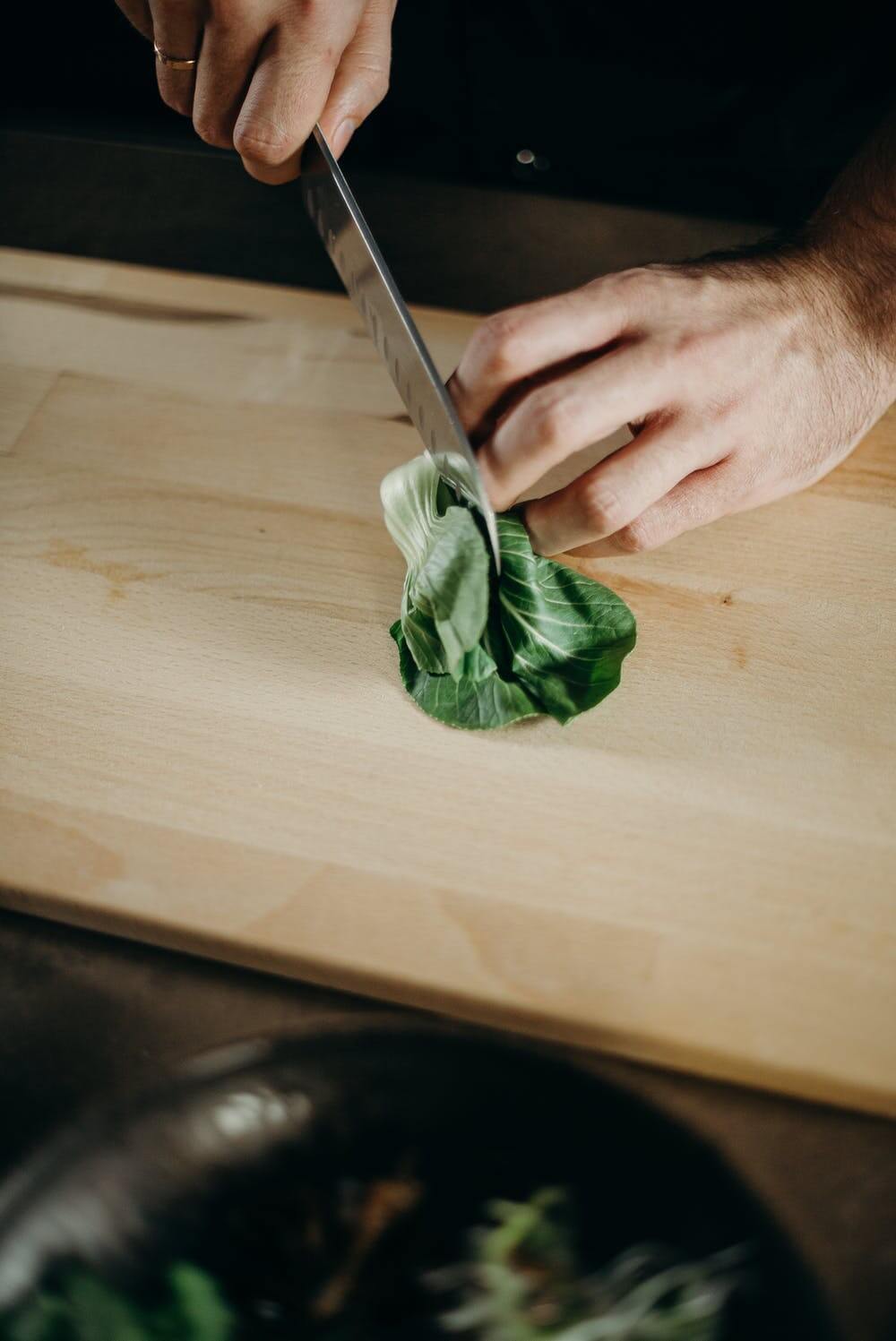 Hands holding a knife cutting bok choy
