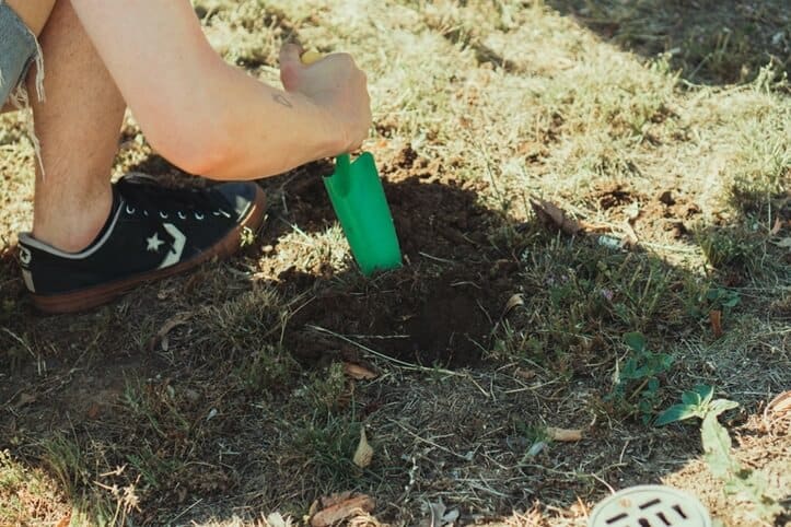 Hand digging a hole with a green shovel